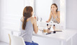 © lenetsnikolai - Amazing young woman doing her makeup in front of mirror. Portrait of beautiful girl near cosmetic table