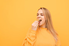 Hungry Attractive Girl Eats A Lot Of French Fries, Holds A Handful Of Snacks And Puts It In The Mouth. Close-up Portrait Of A Girl Greedily Eats French Fries On A Yellow Background