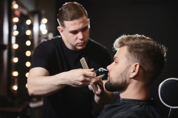 Getting perfect shape. Close-up side view of young bearded man getting beard haircut by hairdresser or barber at barbershop