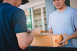 © wutzkoh - Young asian man smiling while delivering a cardboard box to the woman holding document to signing signature.