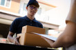 © wutzkoh - Delivery young man standing at the door of home and carrying parcels for young male to signing.