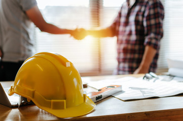 yellow safety helmet on workplace desk with construction worker team hands shaking greeting start up
