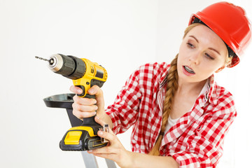 Woman using drill on ladder