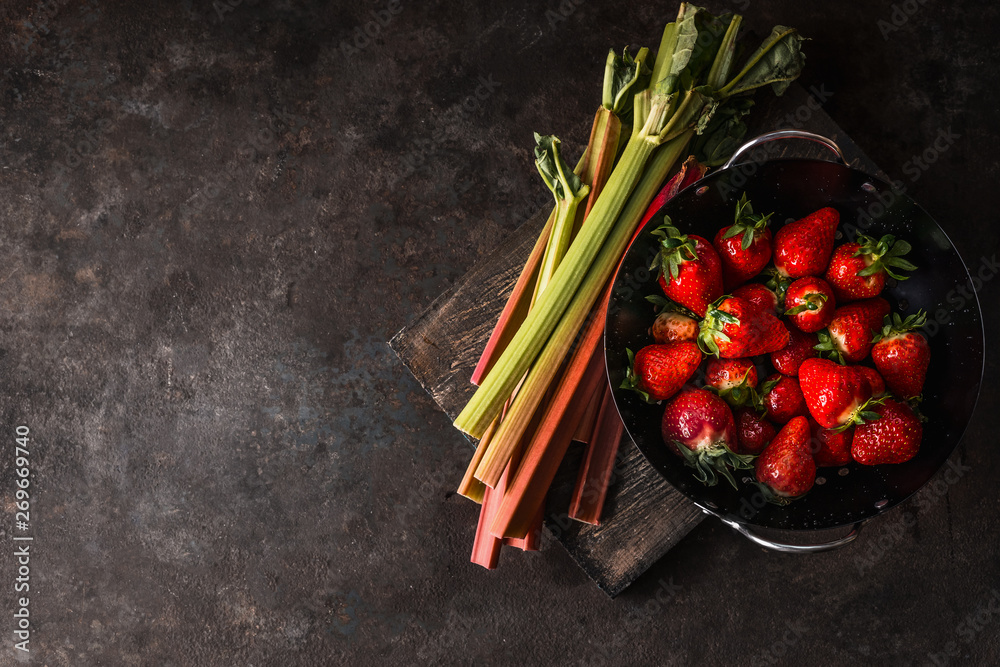 Rhubarb and strawberries on dark rustic kitchen table. Copy space. Seasonal organic food. Healthy eating and cooking - obrazy, fototapety, plakaty 