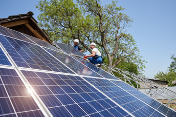 Two technicians on metal platform connecting solar photo voltaic panels on bright sunny day. Stand-alone solar panel system installation, efficiency and professionalism concept.