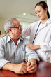 © DragonImages - Senior man in eyeglasses sitting at the table and talking to his doctor while she standing and embracing him