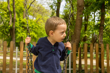 Little cute boy having fun on chain swings at the playground in a sunny spring day.