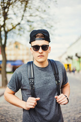 Wall Mural - Hipster style guy. handsome guy with glasses and a fashionable hairdo. vintage photo. The guy standing near the old wooden wall. In the hands of a fashion backpack and a lion, sunglasses