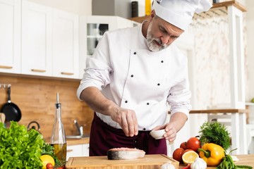 The chef prepares fresh fish salmon, trout, sprinkles with sea salt and vegetables. Horizontal photo. Concept cooking healthy and vegan cuisine, clean food, restaurants, hotel business.