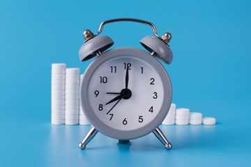 Wall Mural - clock with alarm clock stand on a blue background and show the exact time for the taking of medicines next to them; medical talbetas are laid out for the treatment of diseases