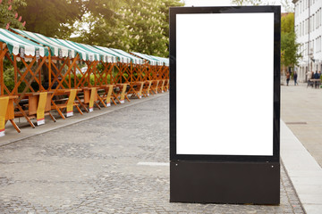 City format. Vertical lightbox with white mock up space for your announcement, advertisement or promotion standing at sidewalk on calm street during daytime. City billboard for posters near road.