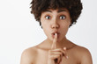© Cookie Studio - Close-up shot of cute and tender feminine african american woman about to tell beauty secret saying shh while showing shush gesture with index finger over mouth gazing friendly at camera