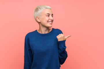 Teenager girl with white short hair over pink wall pointing to the side to present a product