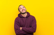 © luismolinero - Colombian man with sweatshirt over yellow wall looking up while smiling