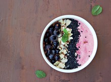 Smoothie Bowl Based On Mashed Berries, Banana And Natural Yogurt In A White Bowl. Decorated With Frozen Blackcurrant, Sliced Almonds And Black Sesame Seeds. Healthy Dessert. Top View, Copy Space.