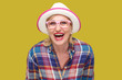 © khosrork - Portrait of happy modern stylish mature woman in casual style with hat and eyeglasses standing and looking at camera with surprised face and laughing. indoor studio shot isolated on yellow background.