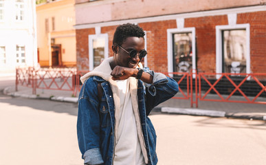 Fashion portrait smiling african man with smart watch using voice command recorder or takes calling walking on city street