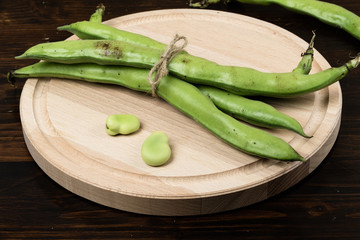 fresh broad beans on wooden cutting board and dark wood table