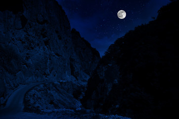 Wall Mural - mountain road through the forest on a full moon night. scenic night landscape of country road at nig