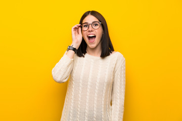 Wall Mural - Young woman over isolated yellow wall with glasses and surprised