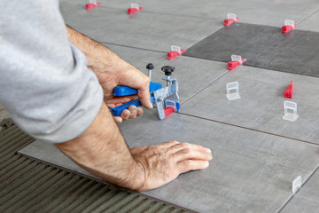 Ceramic Tiles. Tiler placing ceramic wall tile in position over adhesive with lash tile leveling system - Image