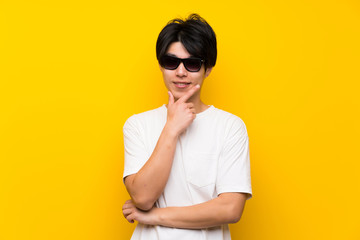 Wall Mural - Asian man over isolated yellow wall with glasses and smiling