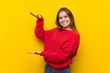 Young woman over yellow wall holding copyspace to insert an ad