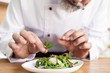 © opolja - male cook chef decorating garnishing prepared salad dish on the plate in restaurant commercial kitchen.