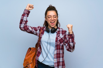 Wall Mural - teenager student girl over isolated blue wall celebrating a victory