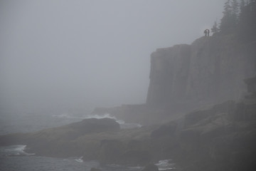 Acadia National Park coastline in the fog with two people silhouetted at the top of a cliff