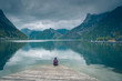 Kobieta samotnie siedzi na drewnianym pomoście nad górskim jeziorem Traunsee w Austrii w pochmurny dzień	