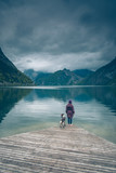 Fototapeta Pomosty - Kobieta z psem Springer Spanielem stoją na drewnianym pomoście nad górskim jeziorem Traunsee w Austrii w pochmurny dzień	