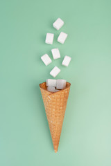 Flying sugar concept. Flying sugar cubes from ice cream cone on green background. Copy space for text. Top view. Vertical arrangement.