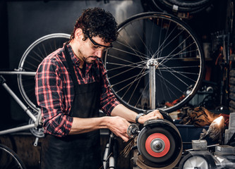 Wall Mural - Skilled repairmaster is working with machine tool at busy bucycle workshop.