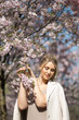 © dissx - Beautiful blonde young woman in Sakura Cherry Blossom park in Spring enjoying nature and free time during her traveling tourist free time - Wearing white pants and t-shirt with a beige jacket