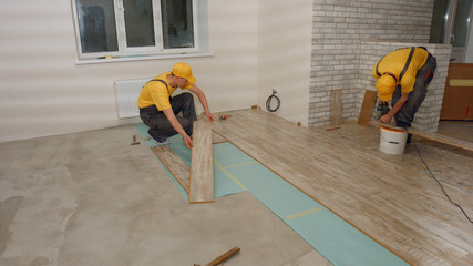 Builders laying wooden laminate boards on floor. Handyman drills board in a new house. Home renovation concept.