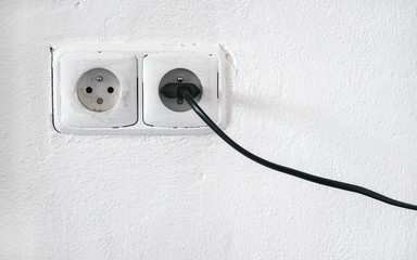 rough facade white wall with two european style power outlet, one socket plugged black cable