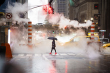 A Woman With An Umbrella And Red High Heels Shoes Is Crossing The 42nd Street In Manhattan. Cars And Steam Coming Out From From The Manholes In The Background. New York City, Usa.