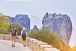 © raisondtre - Hiking young couple tramping on asphalt road in sunset from back. Travel vacation, hiking backpacking, tourism sport and people together concept. Kalambaka, Greece, Monastery Meteora fall view, Europe