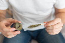 Marijuana Use Concept. Man Preparing And Rolling Marijuana Cannabis Joint. Man Rolling A Cannabis Joint On White Background. Close Up Of Marijuana Joint With Grinder.