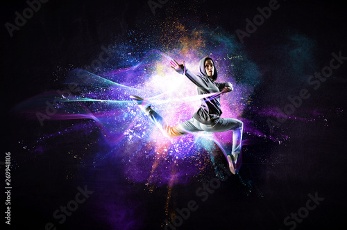Modern female dancer jumping in hoodie with colourful splashes background. Mi...