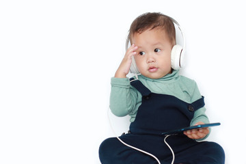 Adorable Asian little baby boy enjoys listening music with headphones by smartphone isolated over white background.