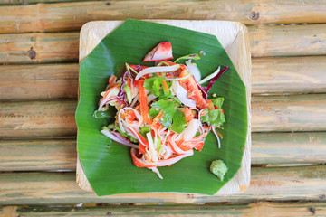 Wall Mural - Thai spicy seafood salad served on banana leaf on bamboo wooden table.