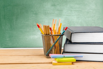 Pile of books with notes paper and pen with pencils in basket container on wooden table with chalkboard background