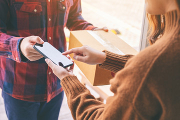 woman receiving parcel box and signing name on the phone from delivery man at the house's door