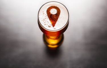 Local beer concept. Location pin symbol on beer glass foam on black table, view from above