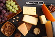 Different types of cheese on a wooden board and other snacks like nuts, fruits.