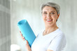 © Pixel-Shot - Sporty mature woman with yoga mat at home