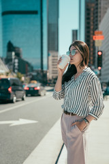 Canvas Print - Professional young urban casual business woman in los angeles city out of concert hall standing on street having hot cup coffee waiting for yellow cab taxi. asian office lady drinking tea for morning