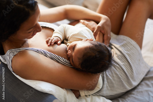Fotografía Close-up of serene loving young black mother in nightgown sitting on bed and bre